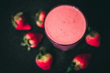 Creamy strawberry smoothie in a glass garnished with fresh strawberries and mint on a wooden table.