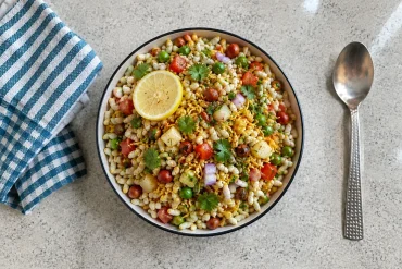 Traditional Indian Jhal Muri made with puffed rice, sev, peanuts, onions, tomatoes, peas, coriander and lemon, served in a bowl.